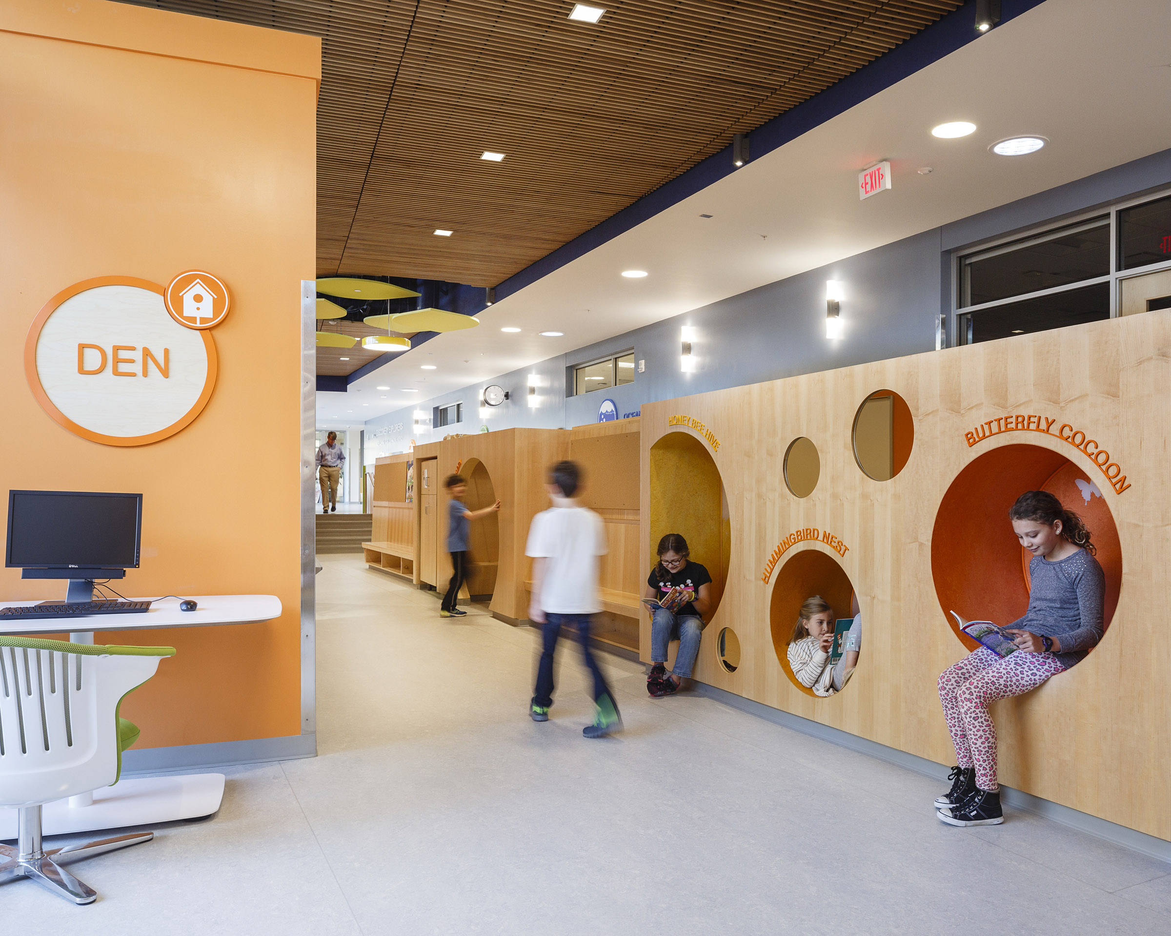 Children play in circular cutouts inside a large, wooden reading nook at Discovery Elementary School