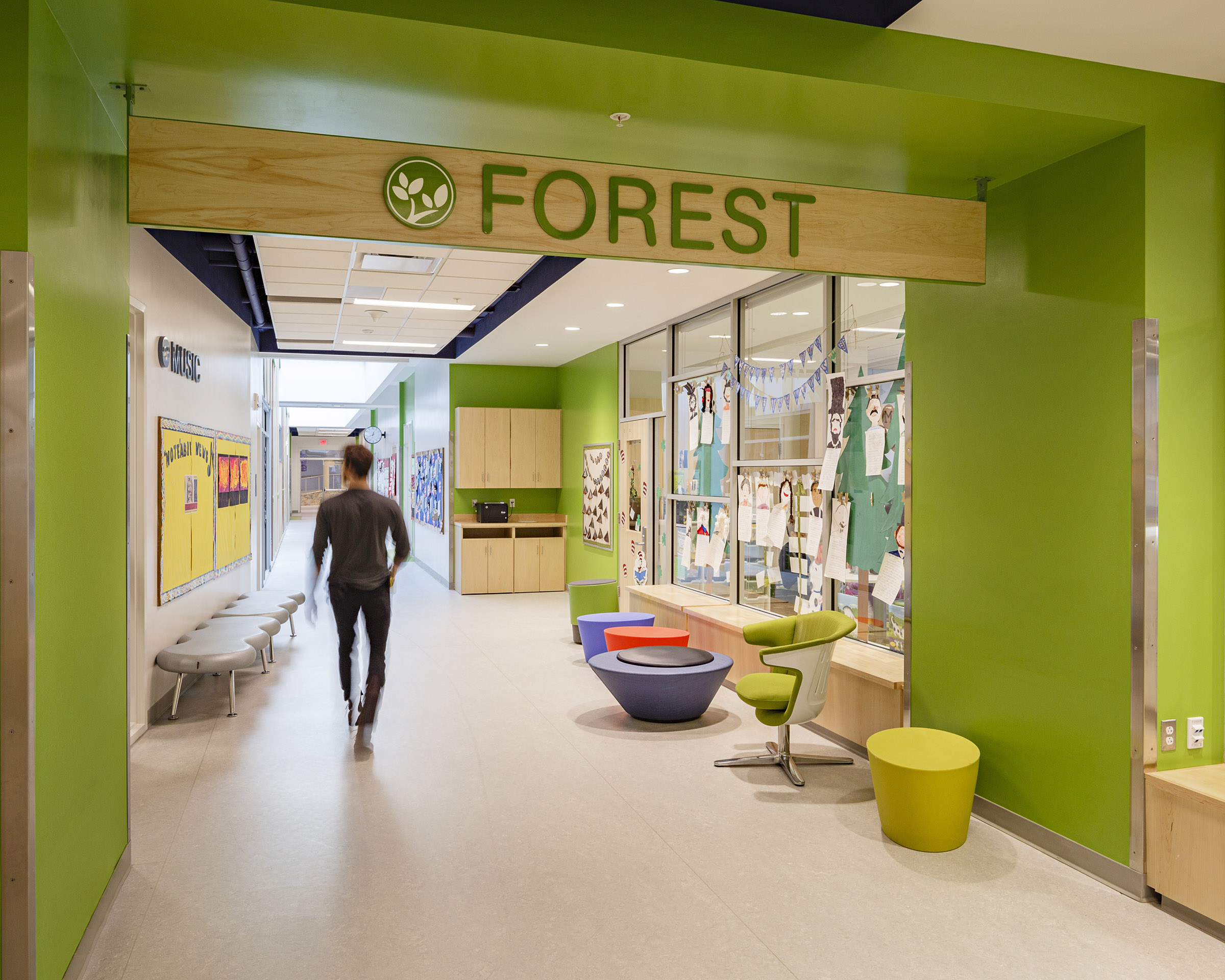 A man walks down a green hallway at Discovery Elementary School with a sign hanging from the ceiling that says "FOREST"