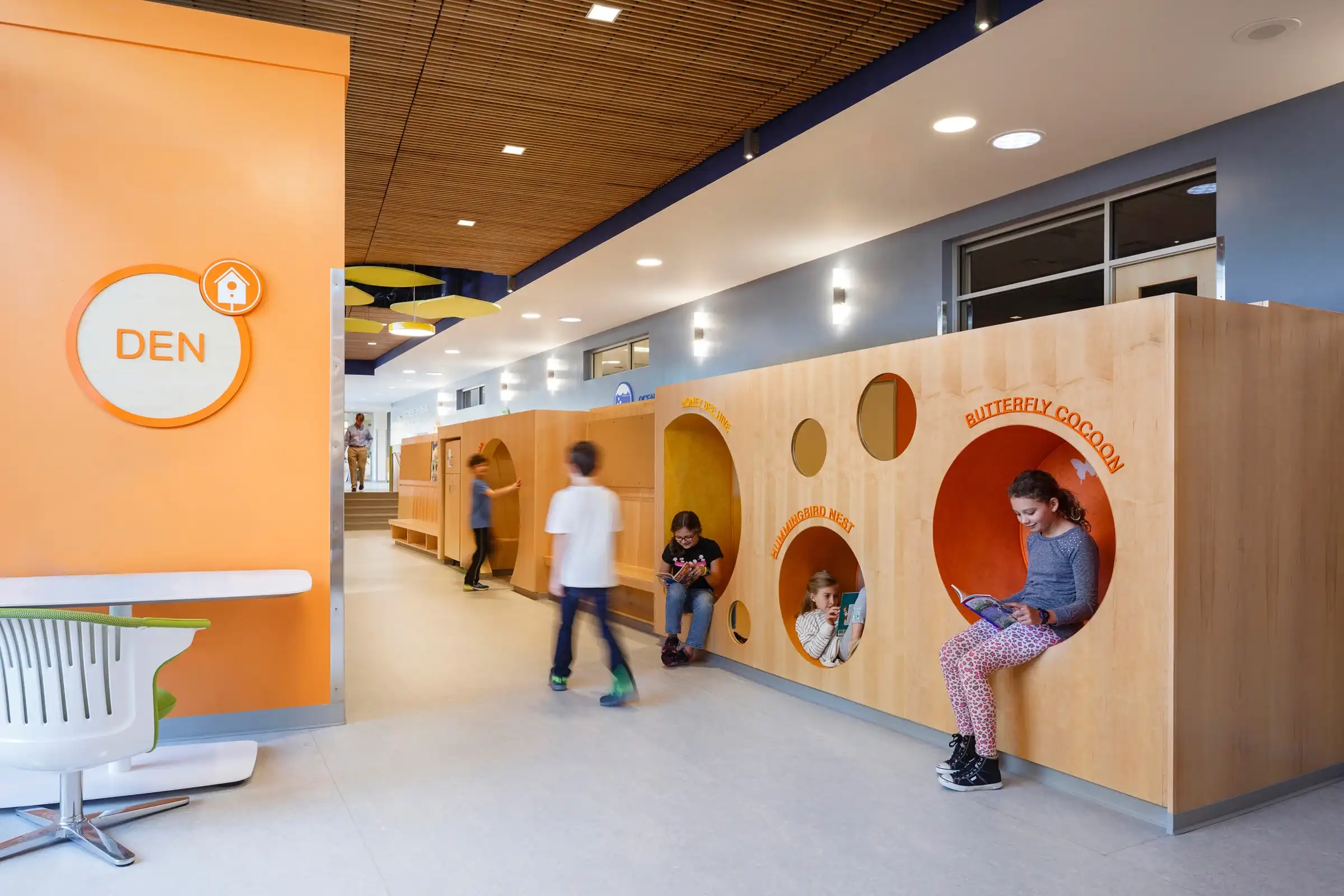 Children play in circular cutouts inside a large, wooden reading nook at Discovery Elementary School