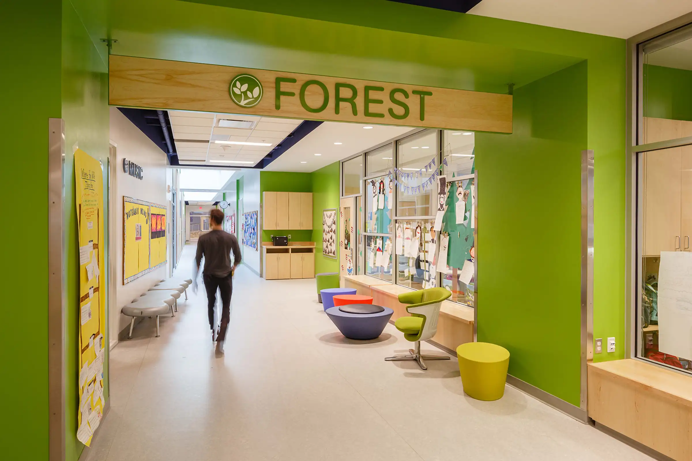 A man walks down a green hallway at Discovery Elementary School with a sign hanging from the ceiling that says "FOREST"
