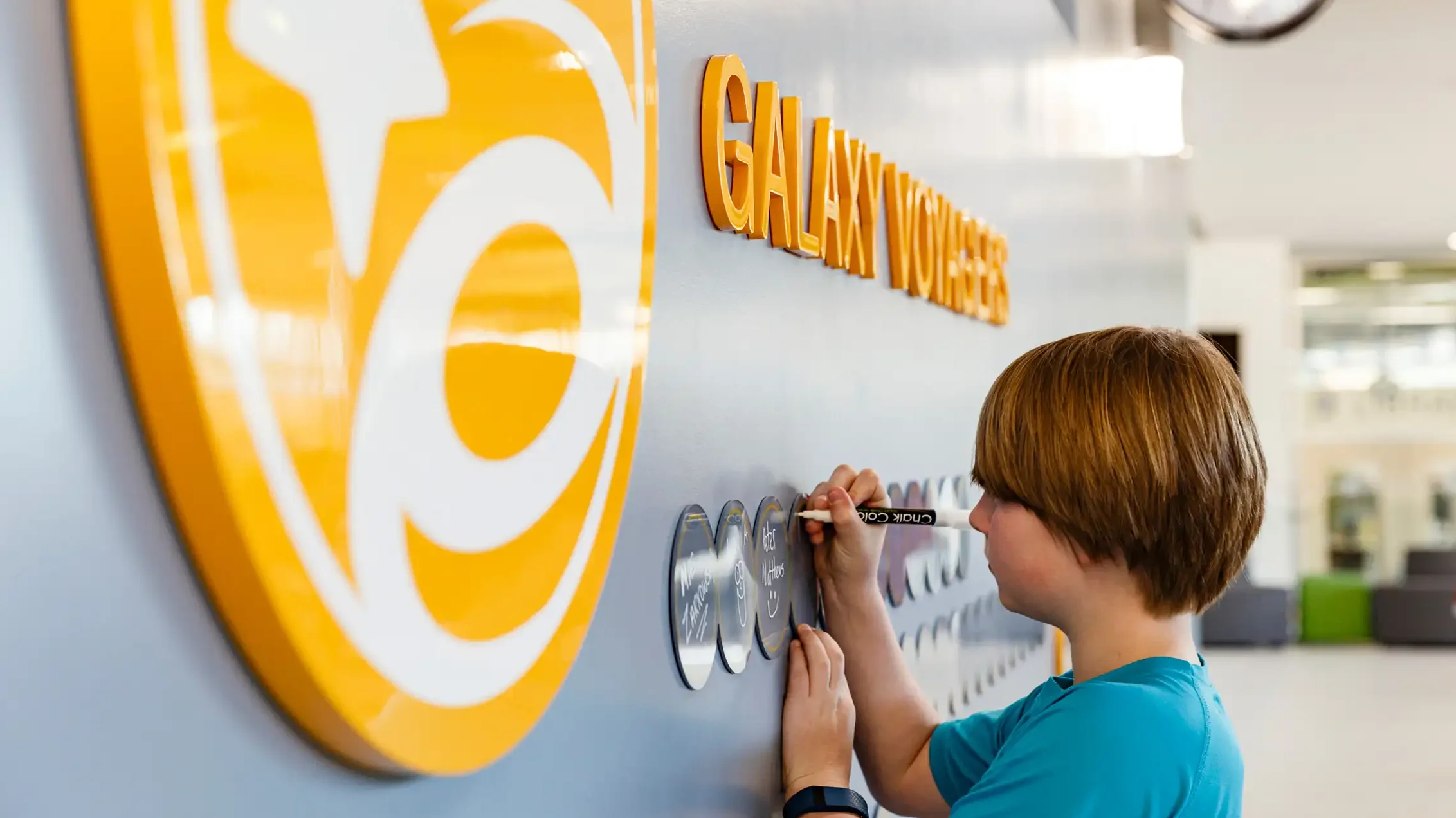A child writes on an acrylic circle on the wall at Discovery Elementary School using a white chalk marker