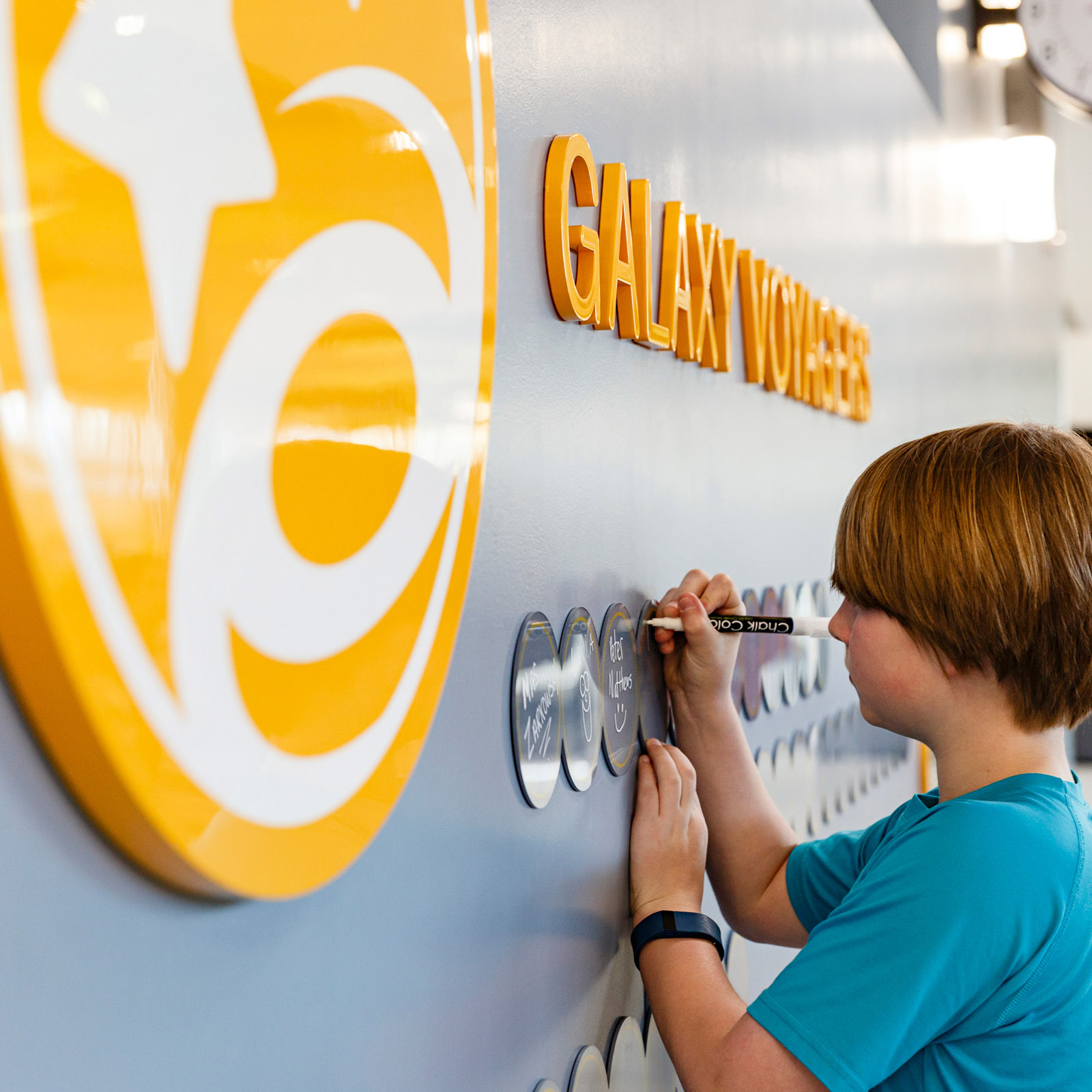 A child writing on an acrylic circle on the wall at Discovery Elementary School with a white chalk marker