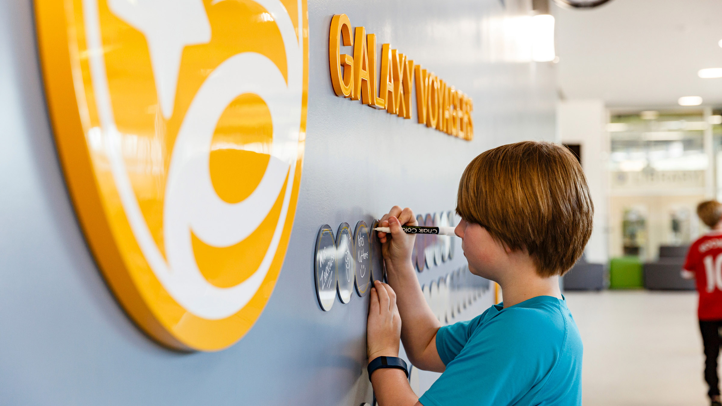 A child writes on an acrylic circle on the wall at Discovery Elementary School using a white chalk marker