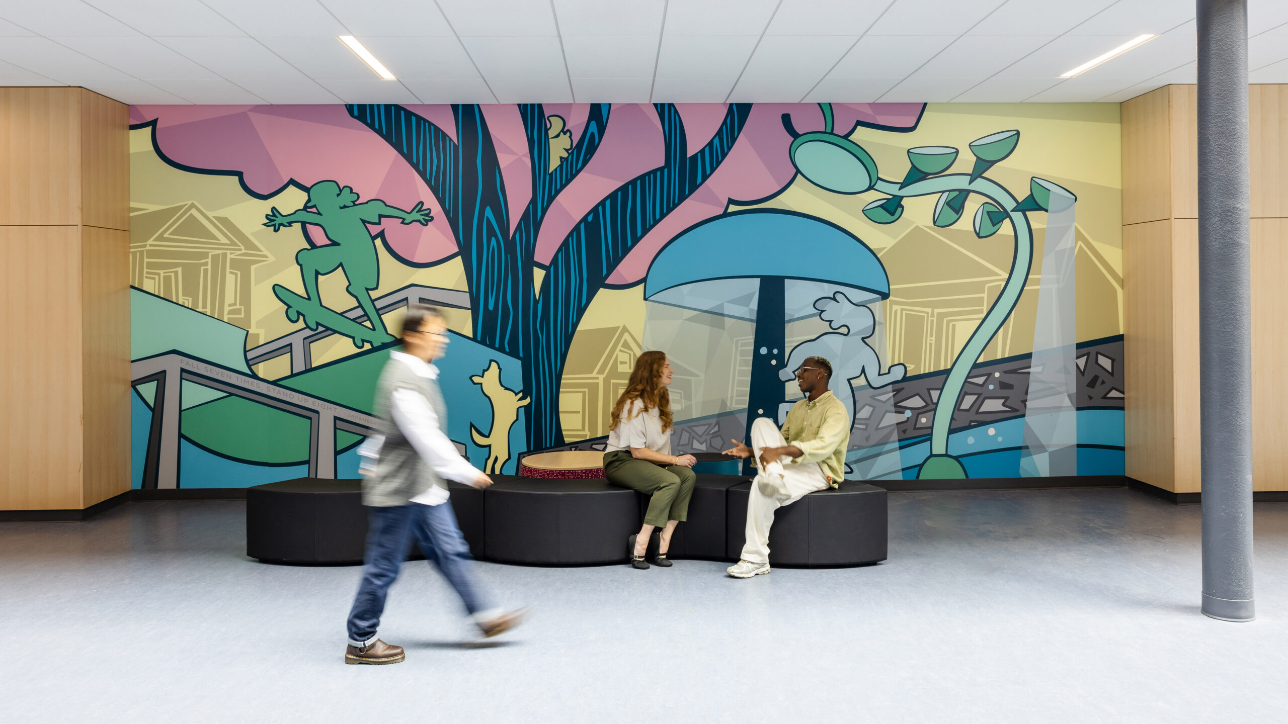 2 people sit in front of a wall mural at Charlottesville Middle School as another person walks past