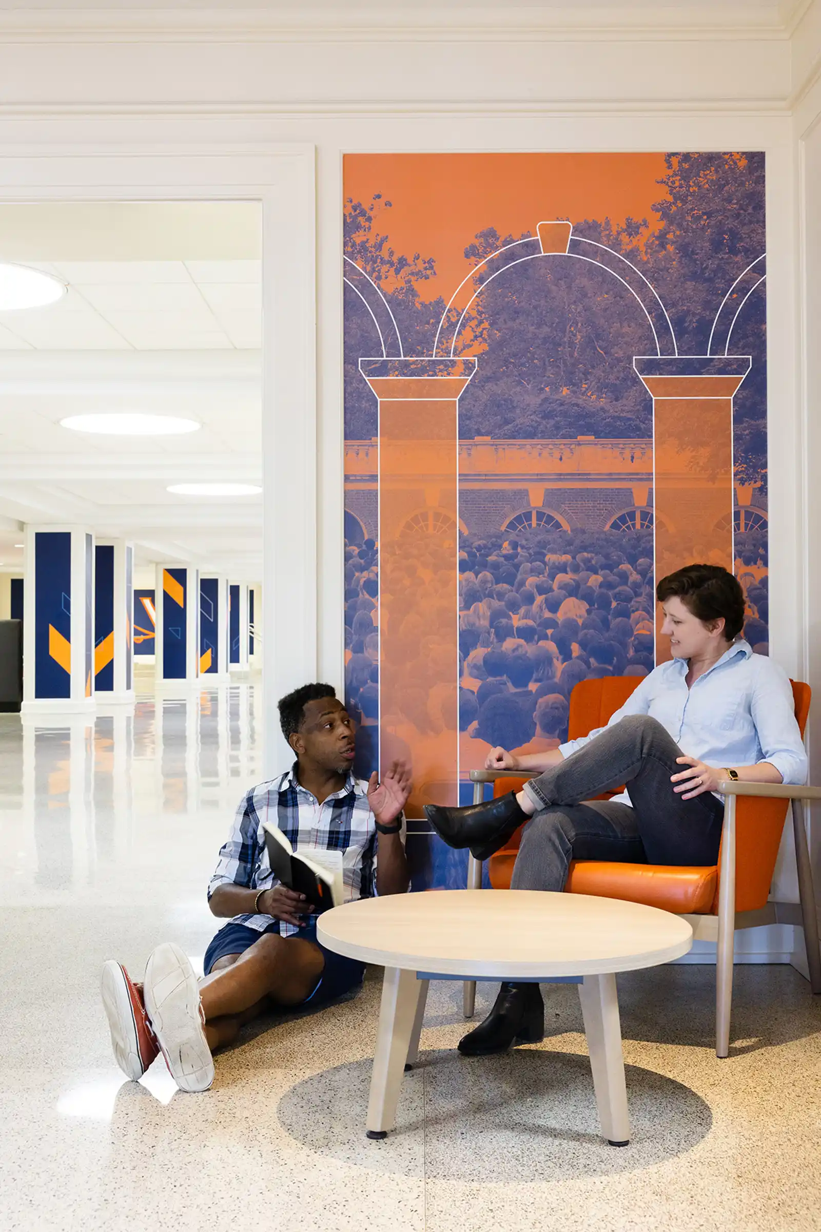 Two people sitting and talking at Newcomb Hall with UVA wall graphics behind them