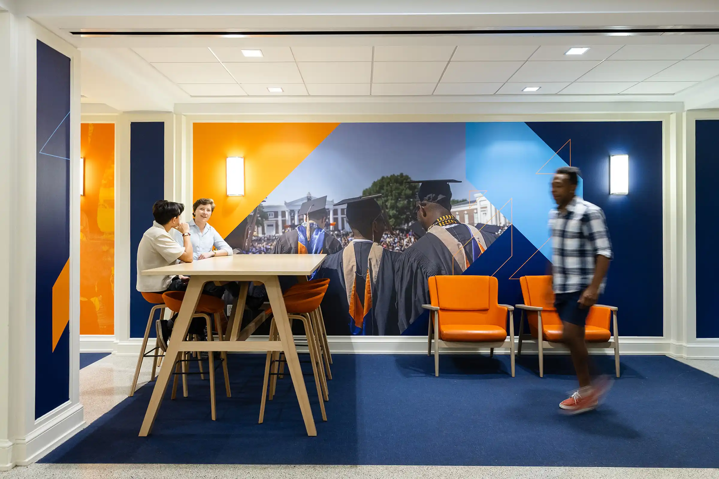 People talking at a table in Newcomb Hall with UVA graphics on the walls around them