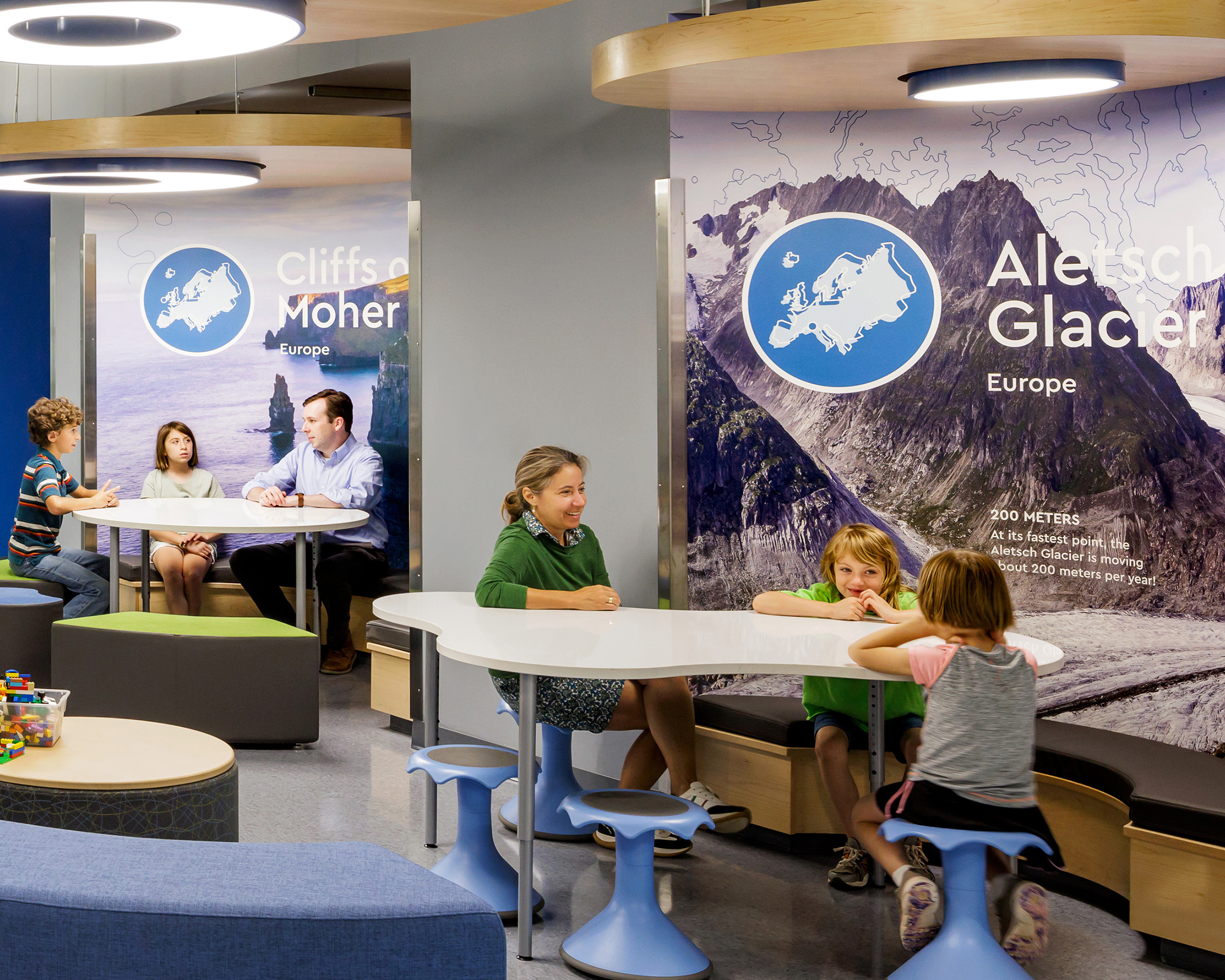 Children learning and playing at tables in front of glacier and cliff wall graphics at Cardinal Elementary School.