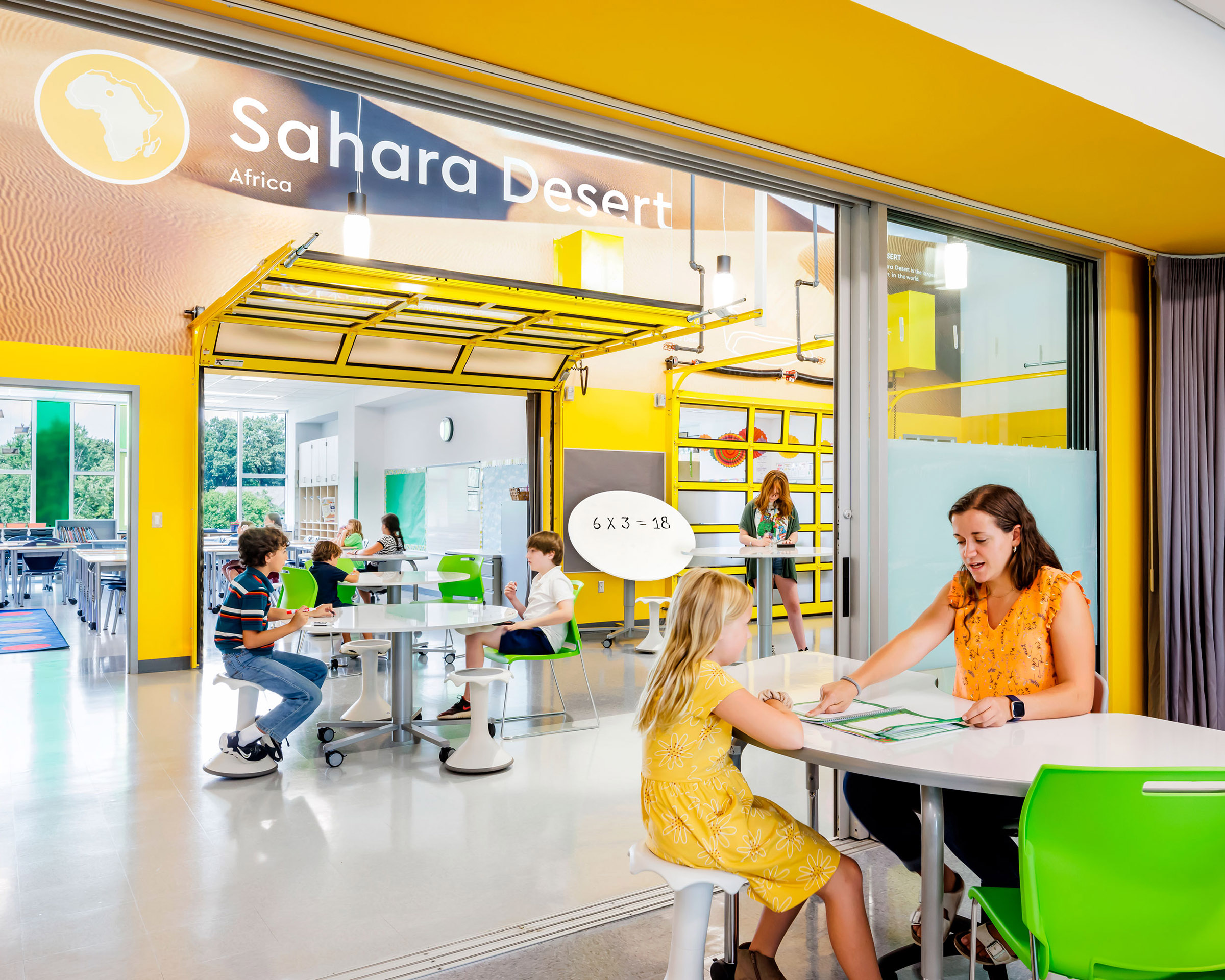Children learning in the "Sahara Desert" section of Cardinal Elementary School with themed wall graphics behind them in yellow.
