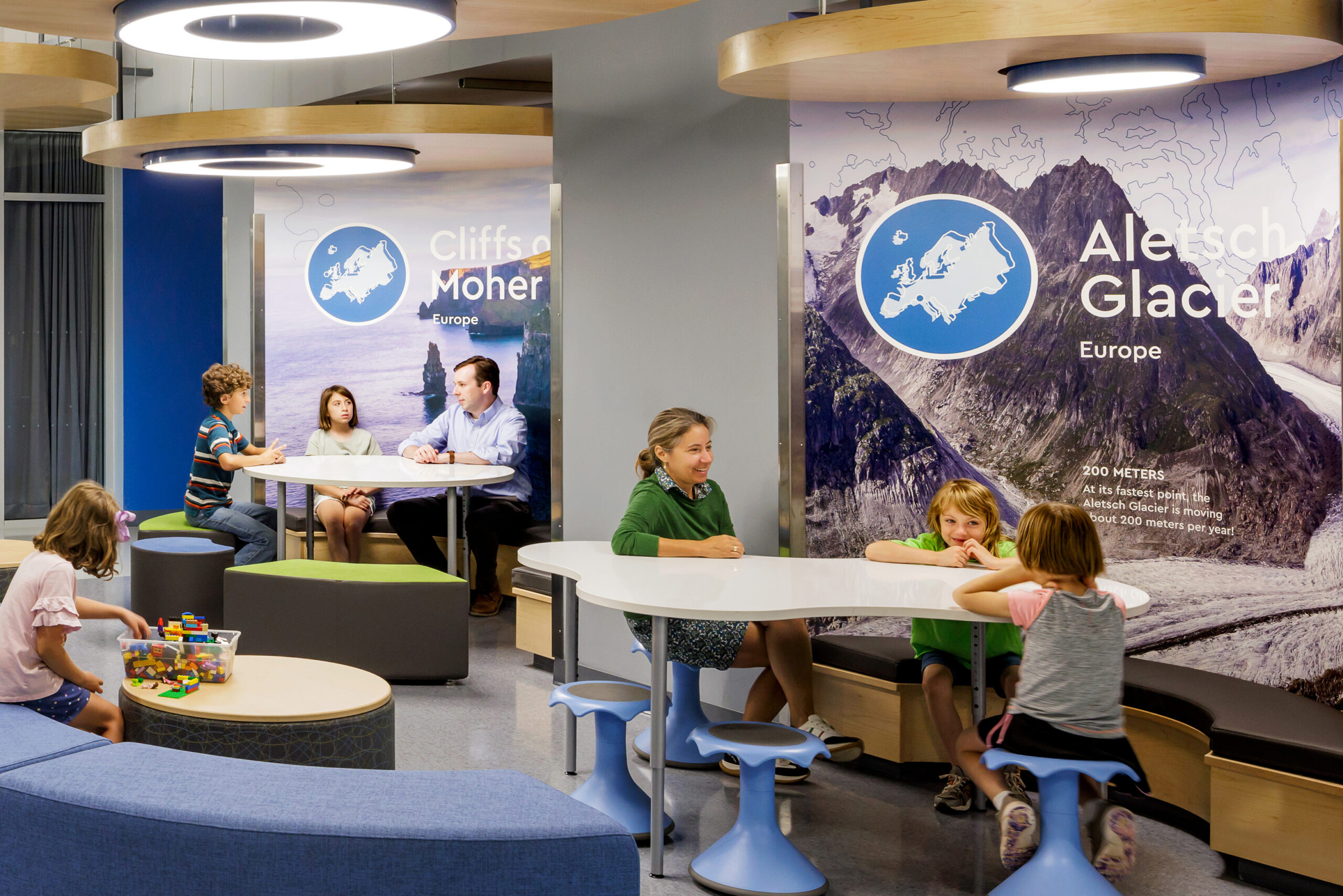 Children learning and playing at tables in front of glacier and cliff wall graphics at Cardinal Elementary School.