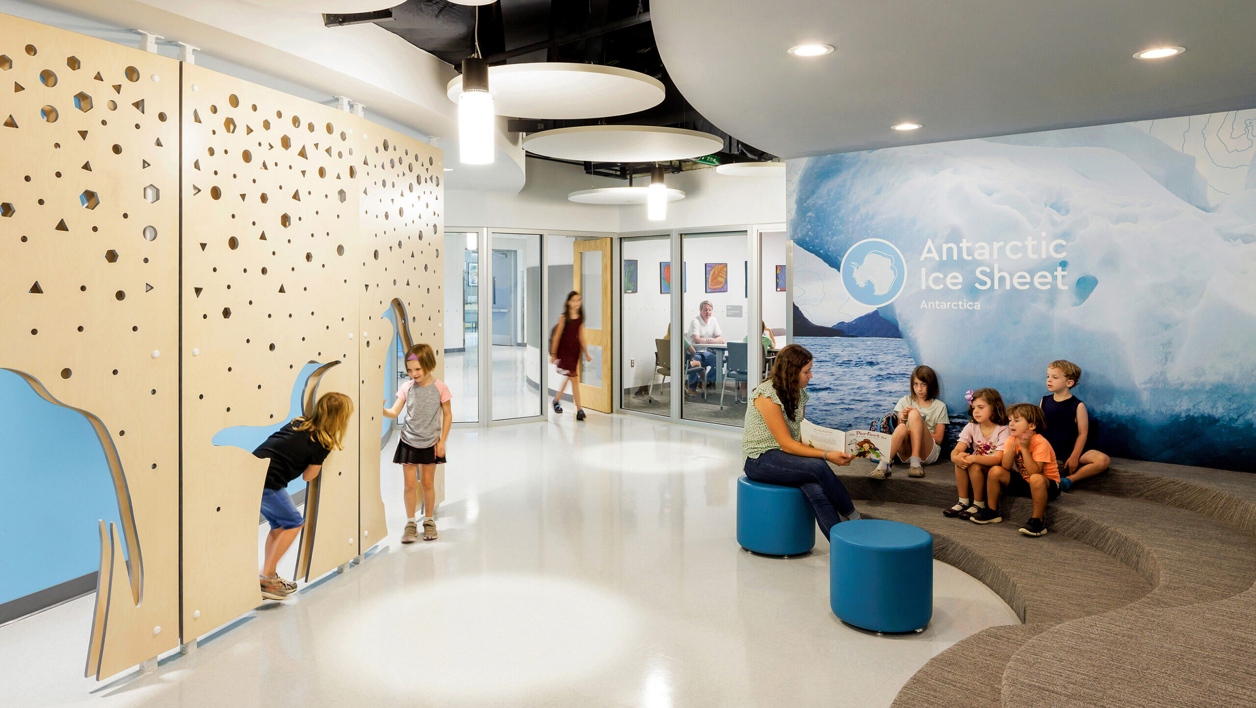 Children play in penguin shaped cut outs of an interactive wall at Cardinal Elementary School across from a graphic wall with the text "Antarctic Ice Sheet"