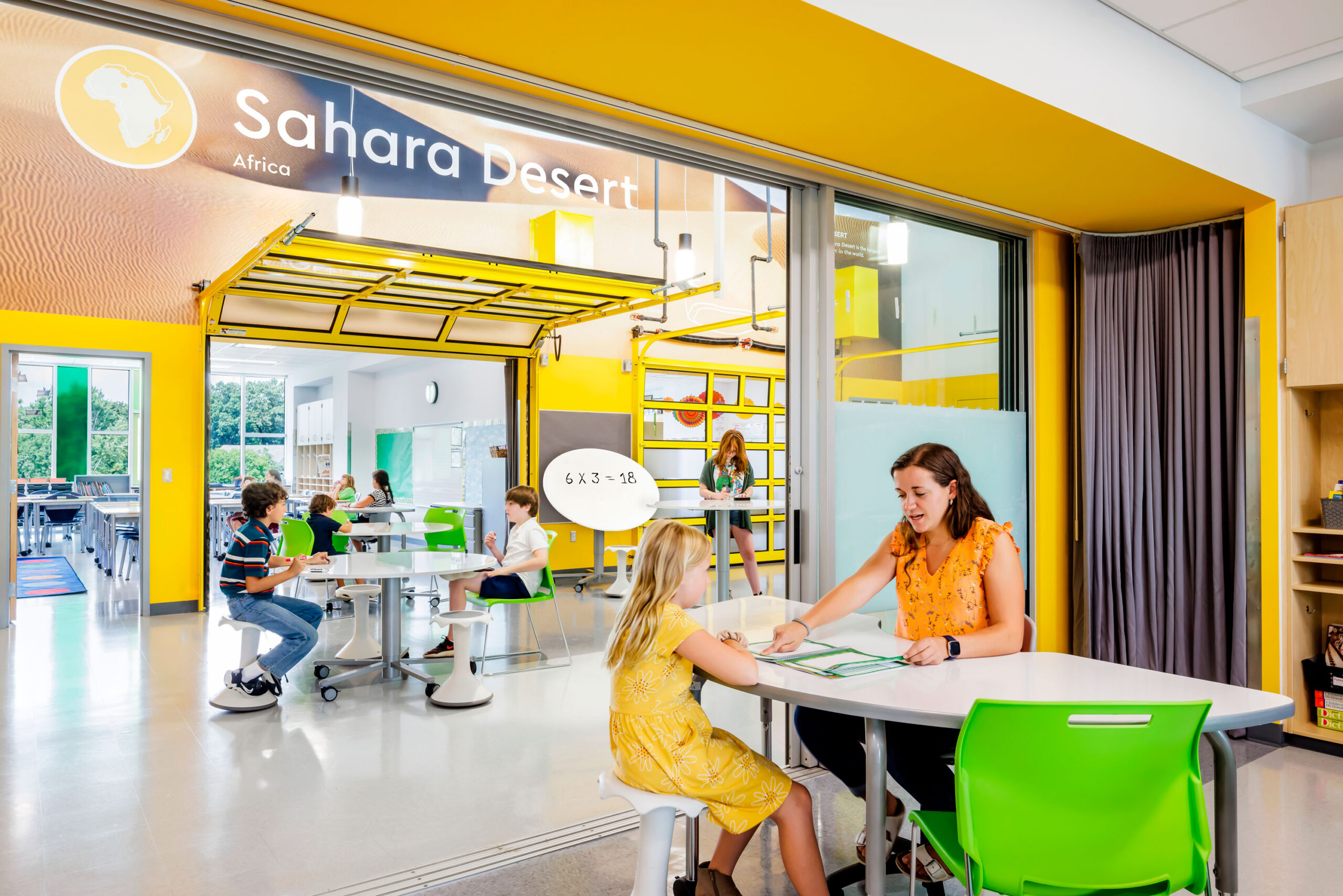 Children learning in the "Sahara Desert" section of Cardinal Elementary School with themed wall graphics behind them in yellow.