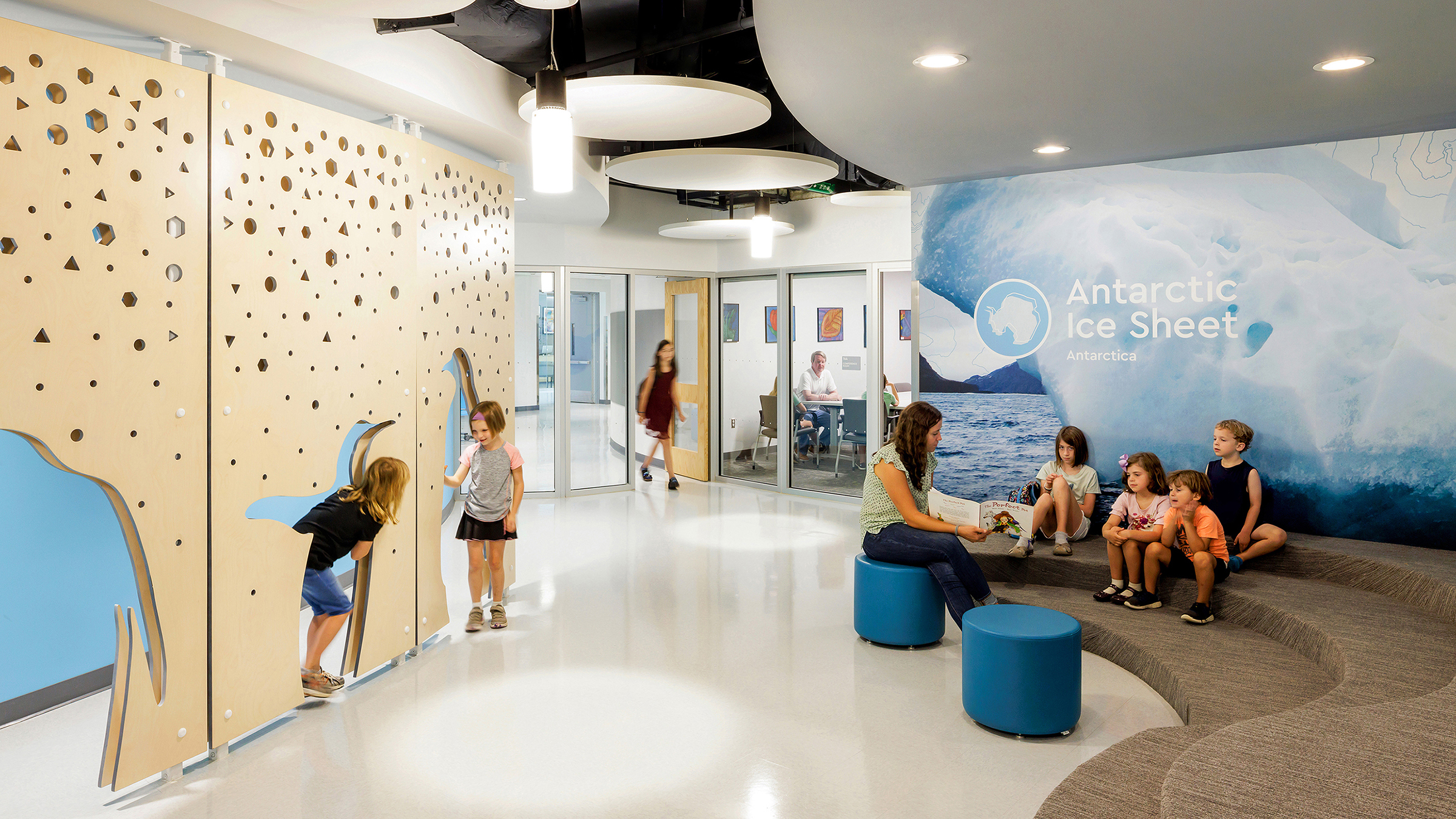 Children play in penguin shaped cut outs of an interactive wall at Cardinal Elementary School across from a graphic wall with the text "Antarctic Ice Sheet"