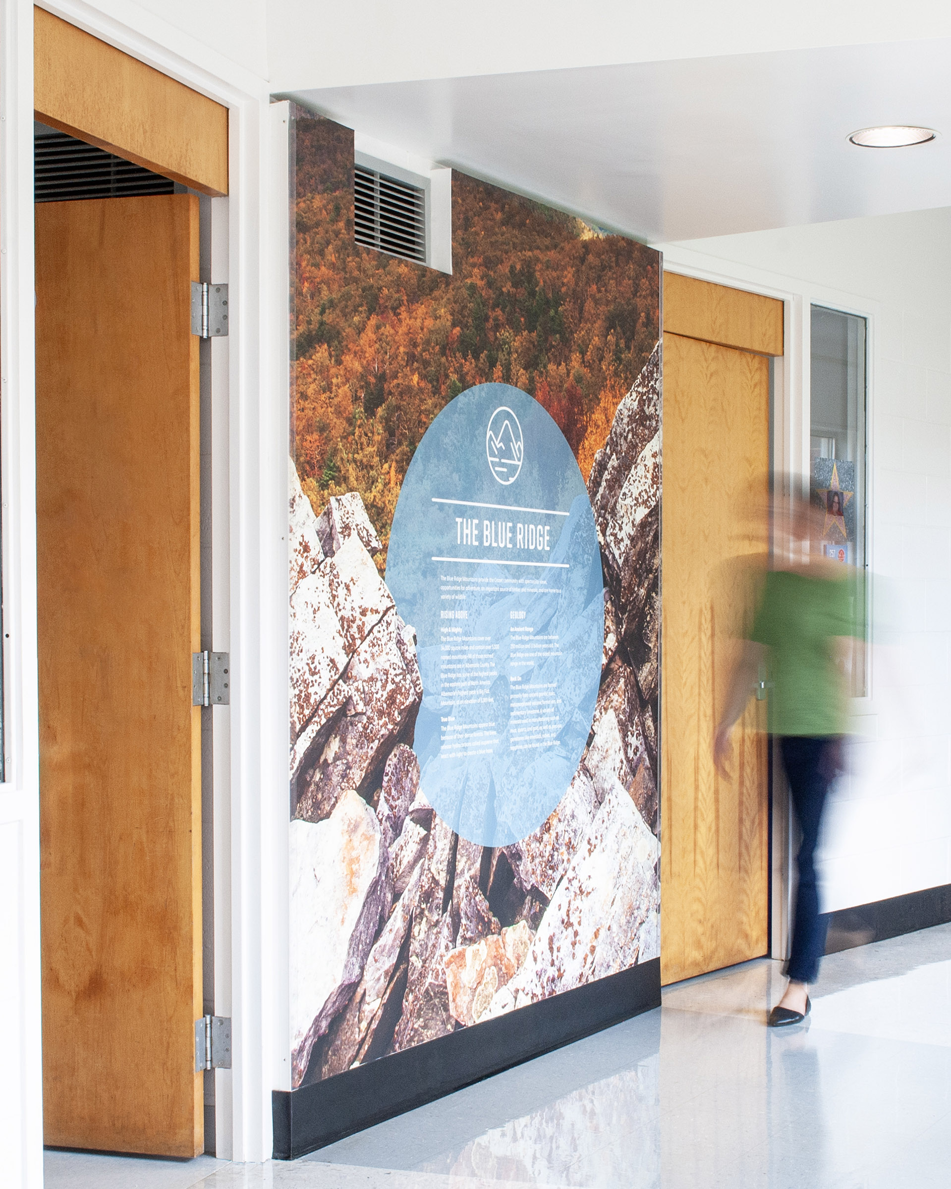 A woman walks by mountain imagery with factoids on the wall at Crozet Elementary School