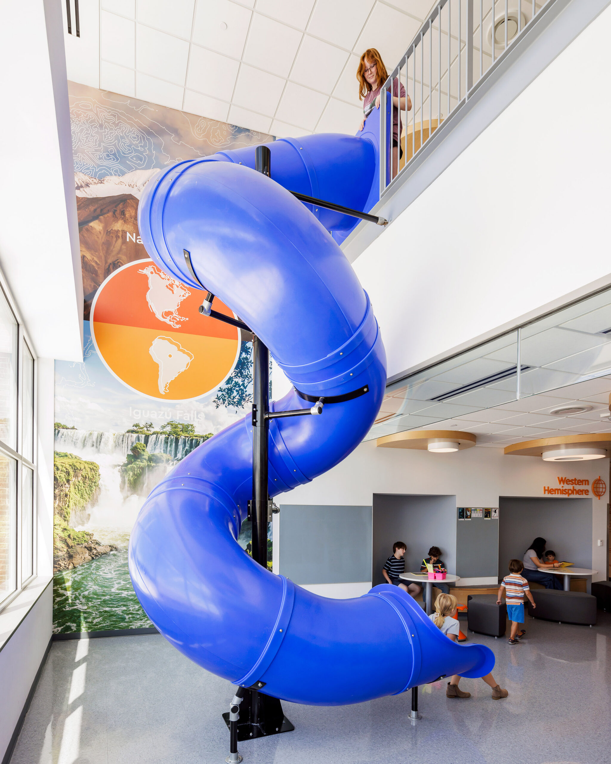 Children playing on an indoor slide at Cardinal Elementary School with wall graphics in the background
