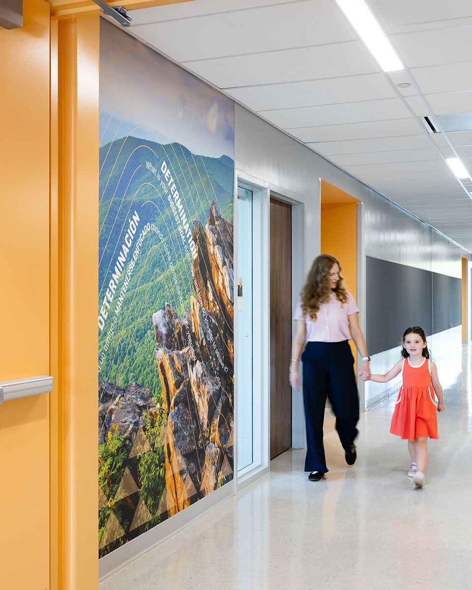 A woman and child walk down the hallway at Mountain View Upper Elementary School with mountain graphics on the left side of the photo.