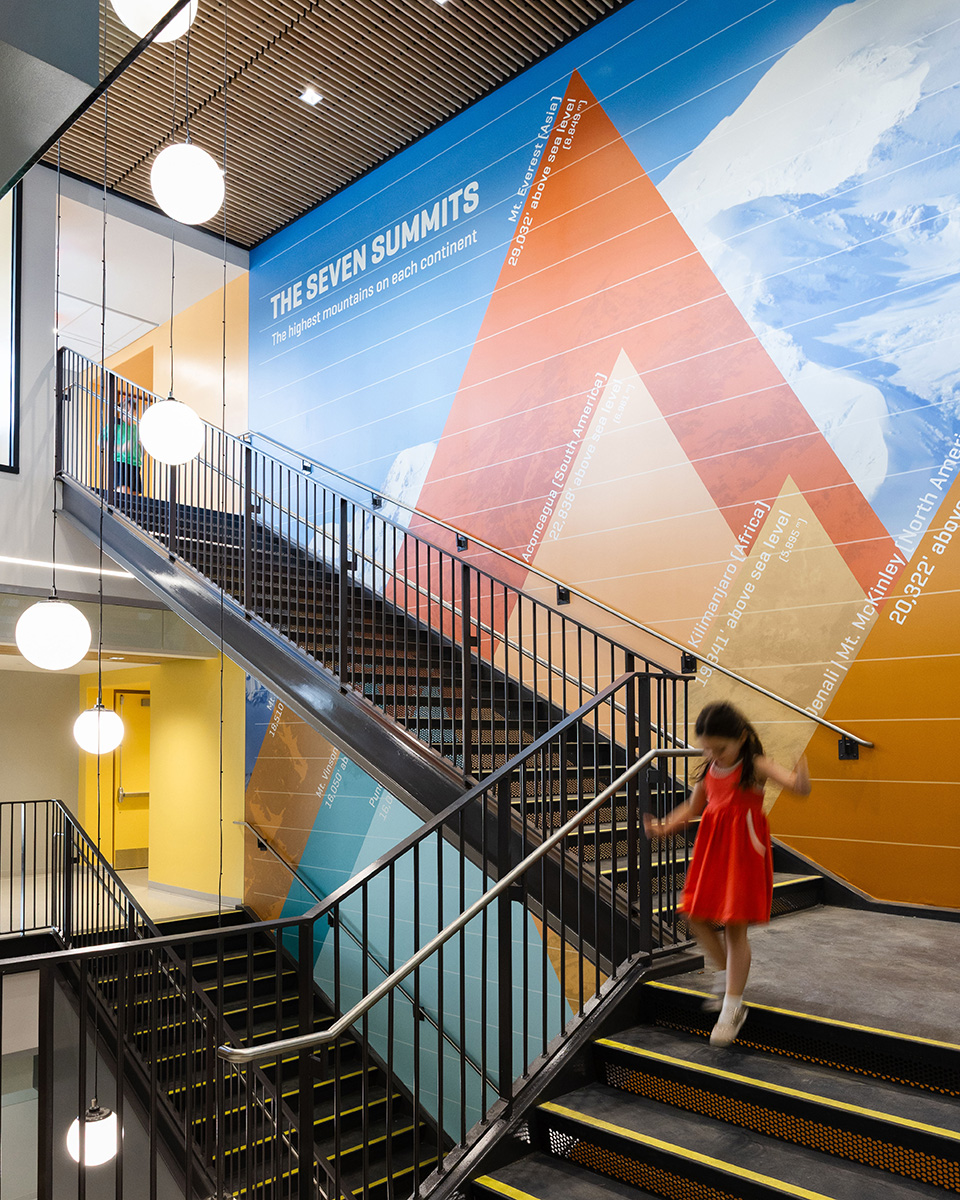A child walks down the stairs at Mountain View Upper Elementary School with mountain graphics on the walls behind her