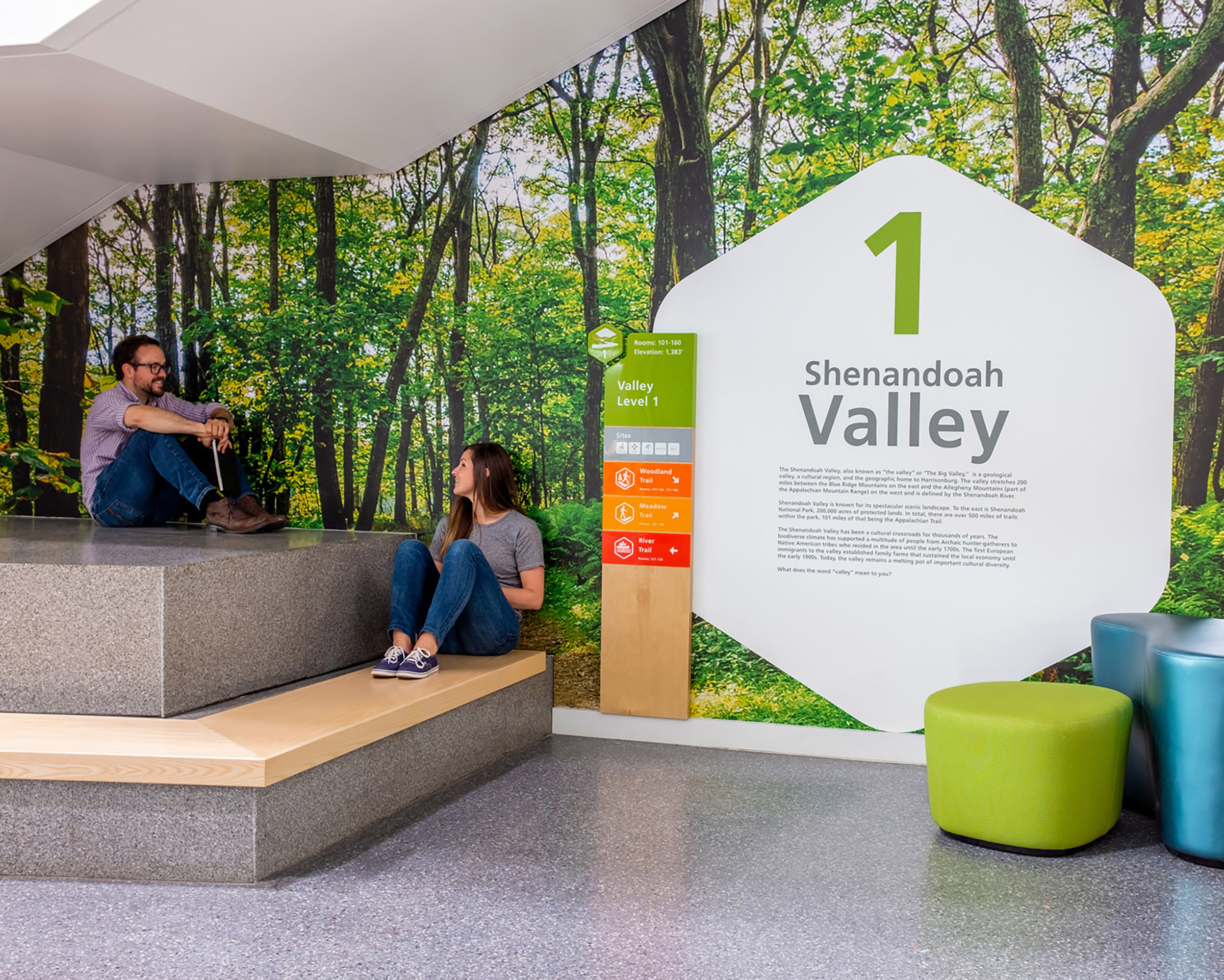 A man and a woman sit in front of wall graphics and wayfinding for floor level 1 at Bluestone Elementary School
