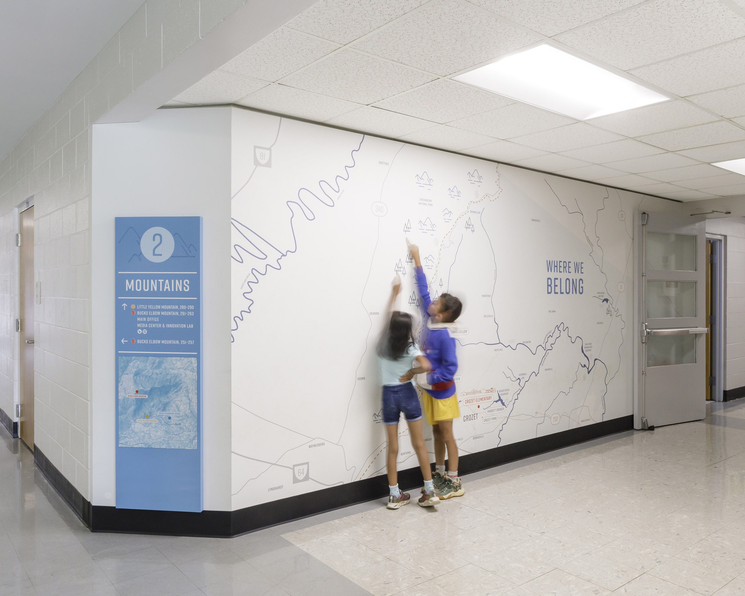 Children interact with a map wall graphic at Crozet Elementary School beside blue wayfinding signage