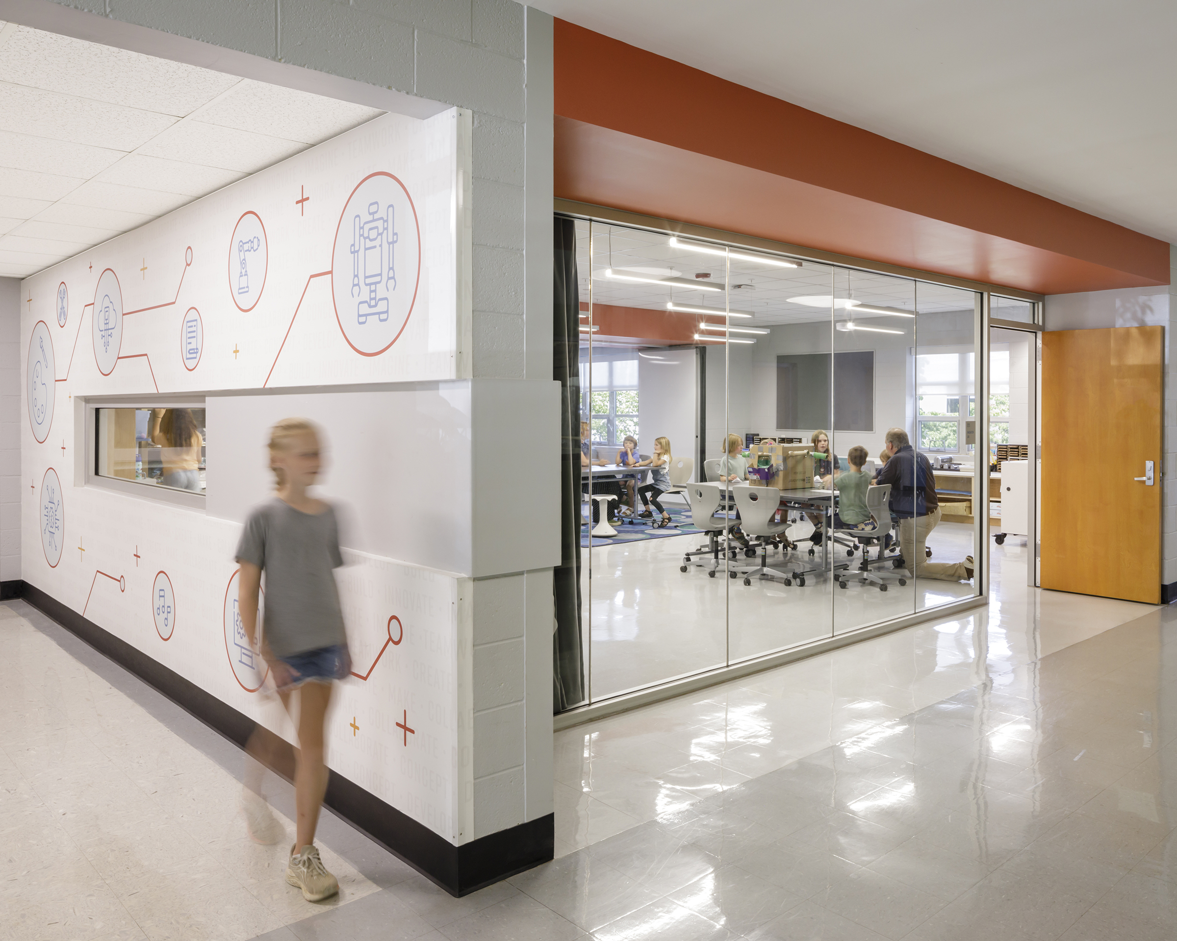 A girl walks down a hallway at Crozet Elementary School with science themed wall graphics behind her in orange and white