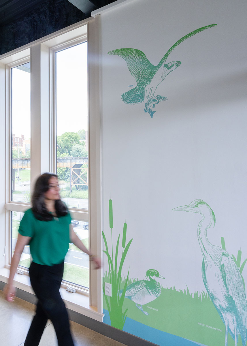 A woman walks by green and blue wall graphics inside JRA Buzzard River Education Center
