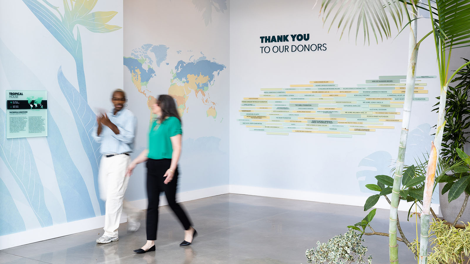 Two people walk by wall graphics and donor signage at Lewis Ginter Botanical Garden