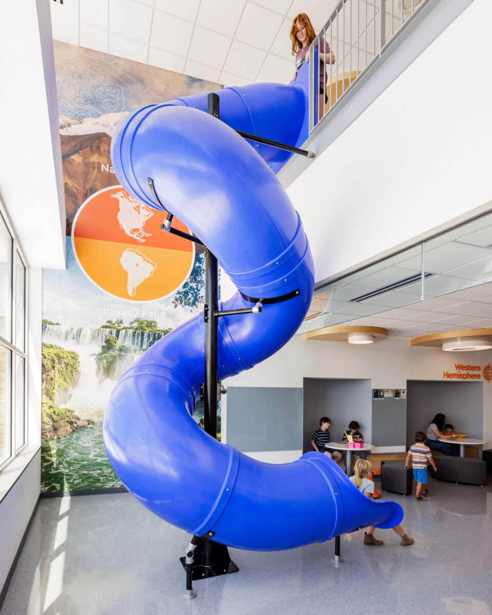 Children playing on an indoor slide at Cardinal Elementary School with wall graphics in the background