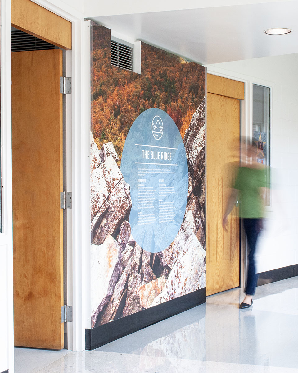 A woman walks by mountain imagery with factoids on the wall at Crozet Elementary School