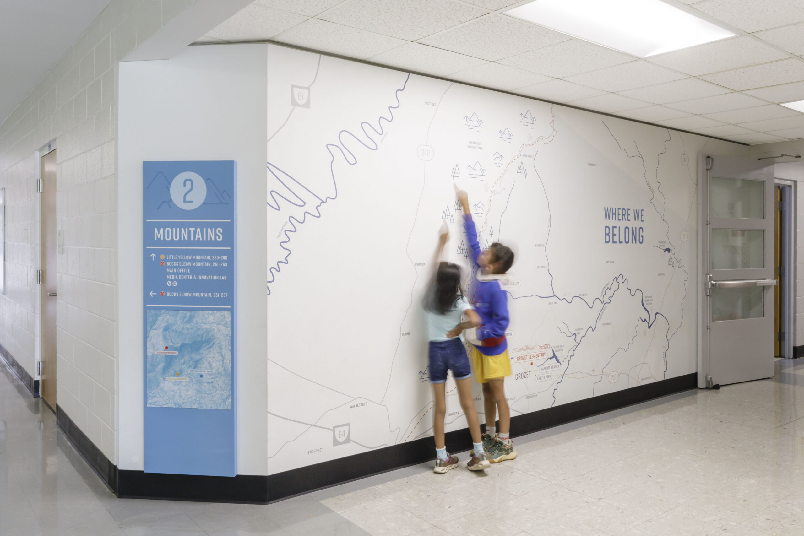 Children interact with a map wall graphic at Crozet Elementary School beside blue wayfinding signage