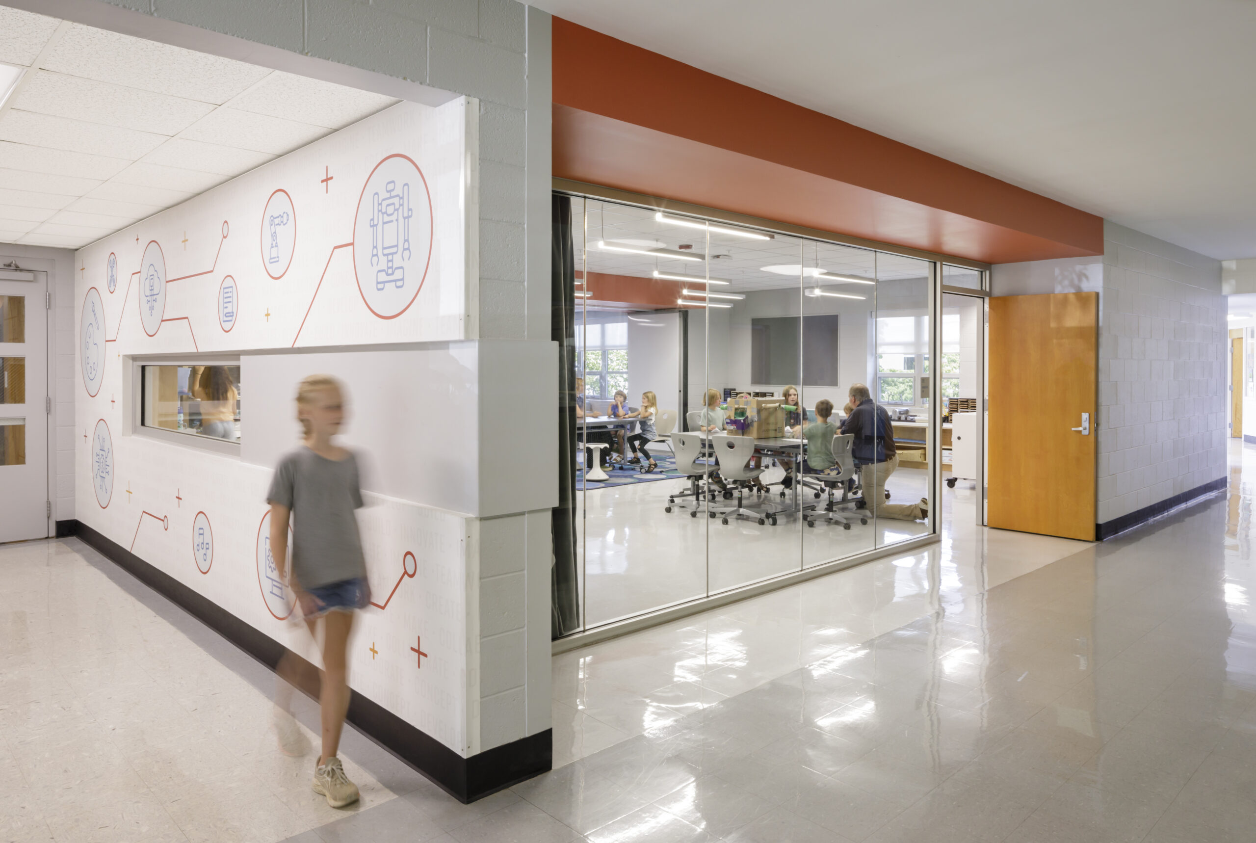 A girl walks down a hallway at Crozet Elementary School with science themed wall graphics behind her in orange and white